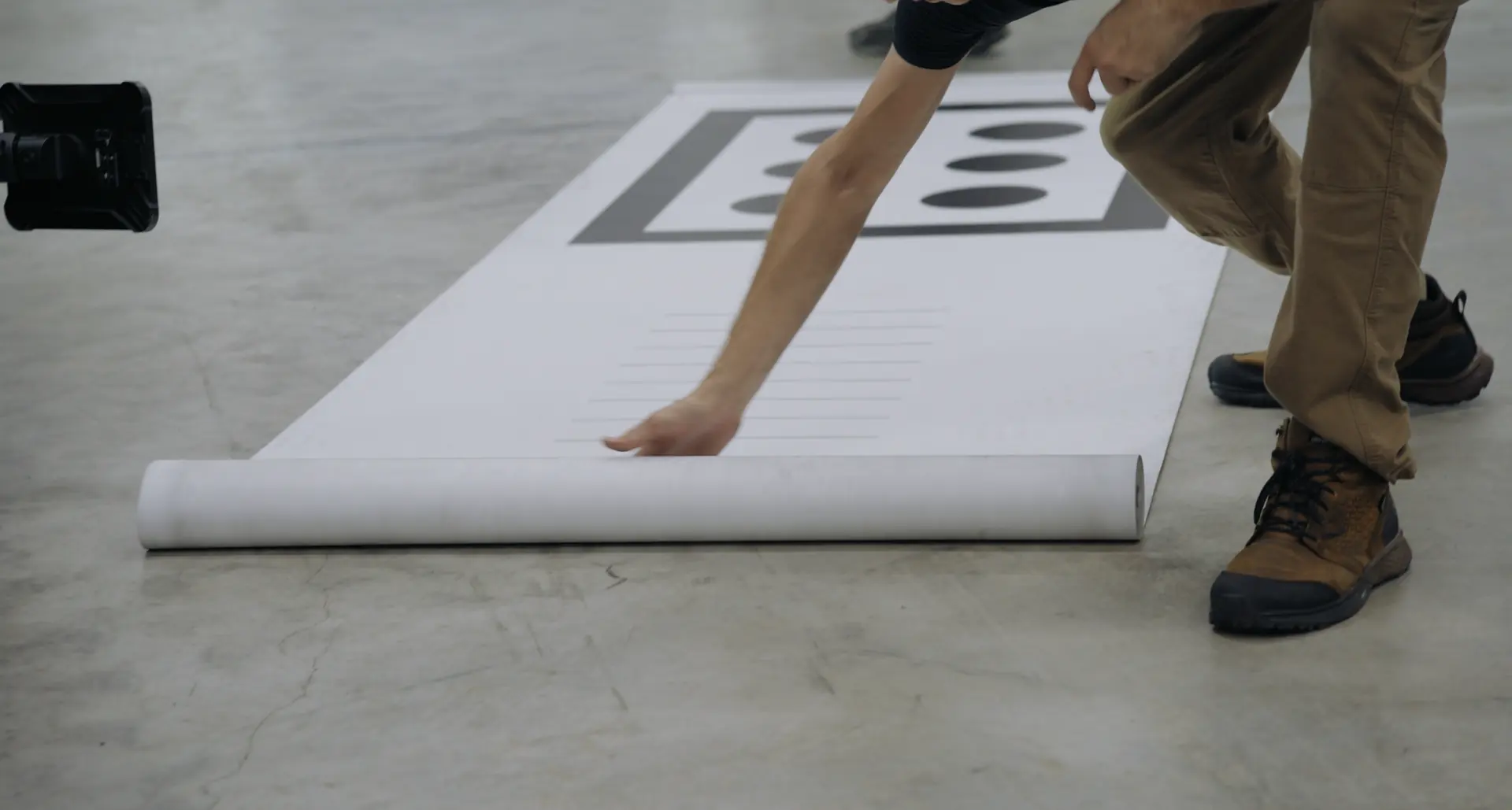 A technician unrolling a large printed floor target across the laboratory floor.