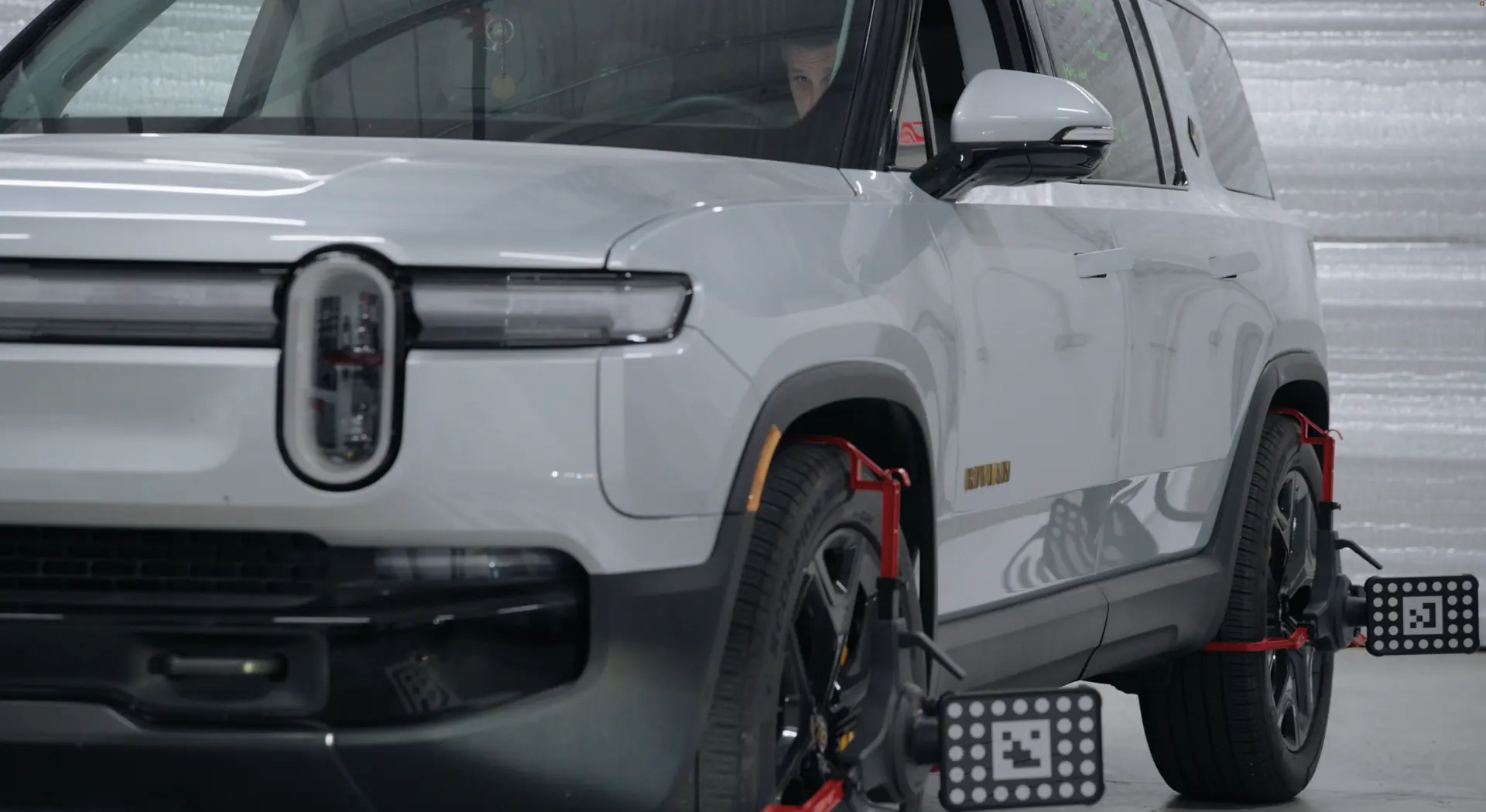 An electric SUV on the alignment rack with calibration targets clamped to its wheels.