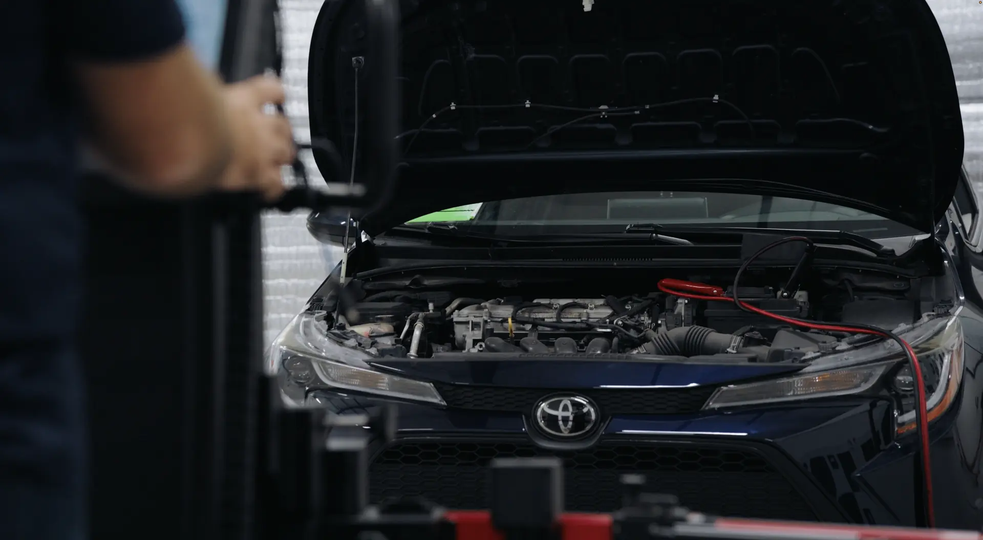 A sedan raised on the rack with its hood open and diagnostic leads connected.