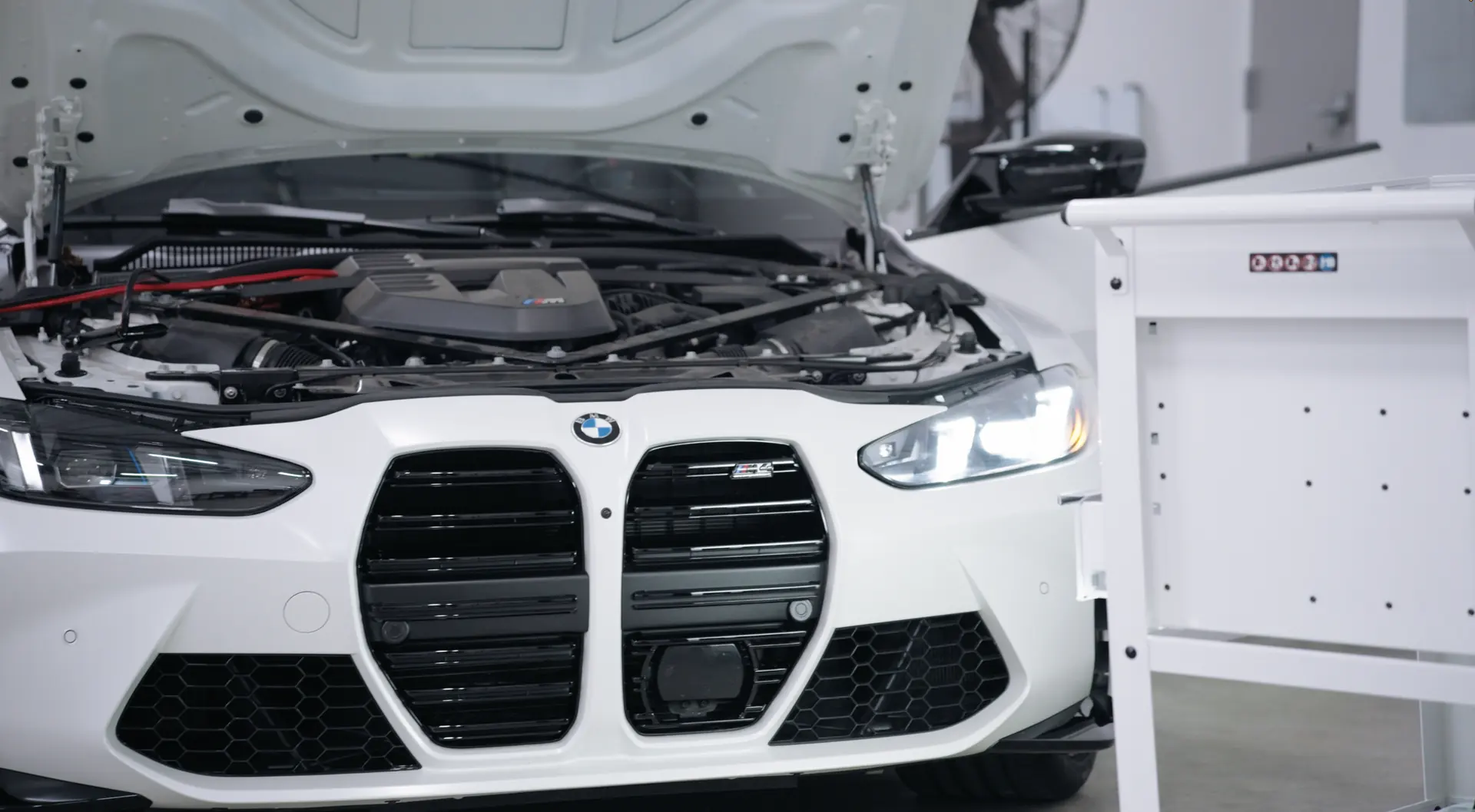 A white performance coupe with its hood open in the calibration laboratory.