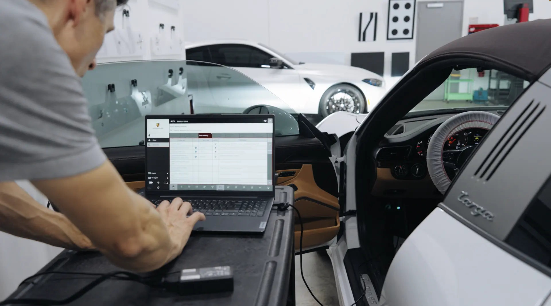 A technician working at a laptop in the open door of a sports car.