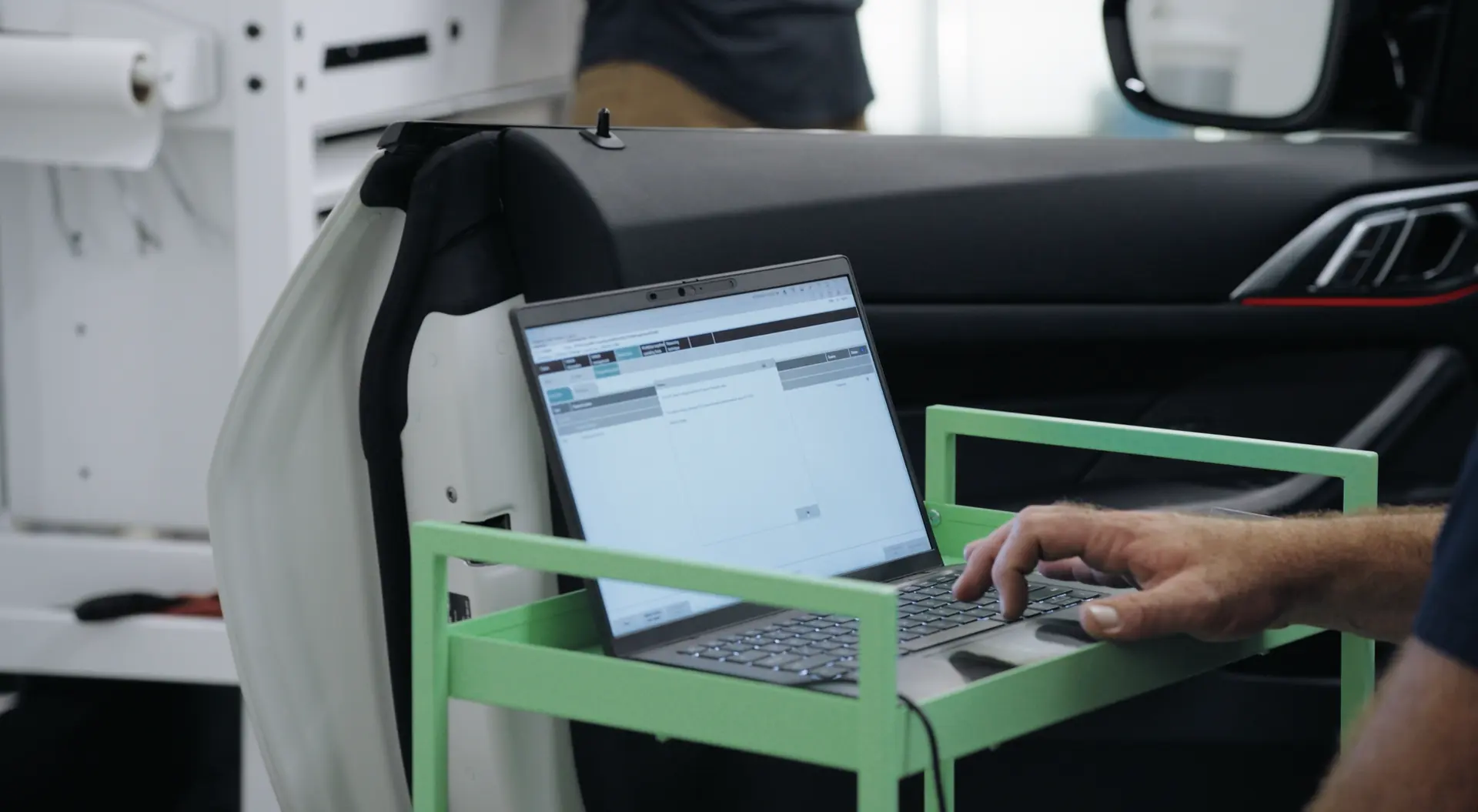 A laptop on a rolling stand cabled into a vehicle during a programming session.