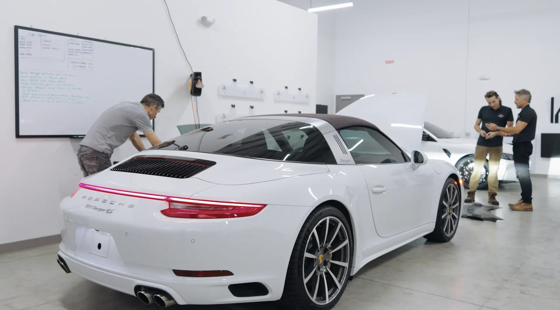 A finished white sports car with two staff members reviewing the job beside it.