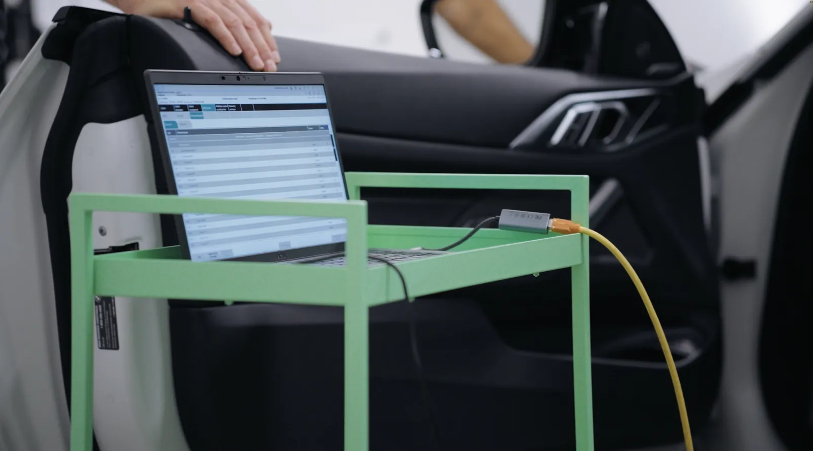 A diagnostic laptop on a rolling stand, cabled into a vehicle through its open door.
