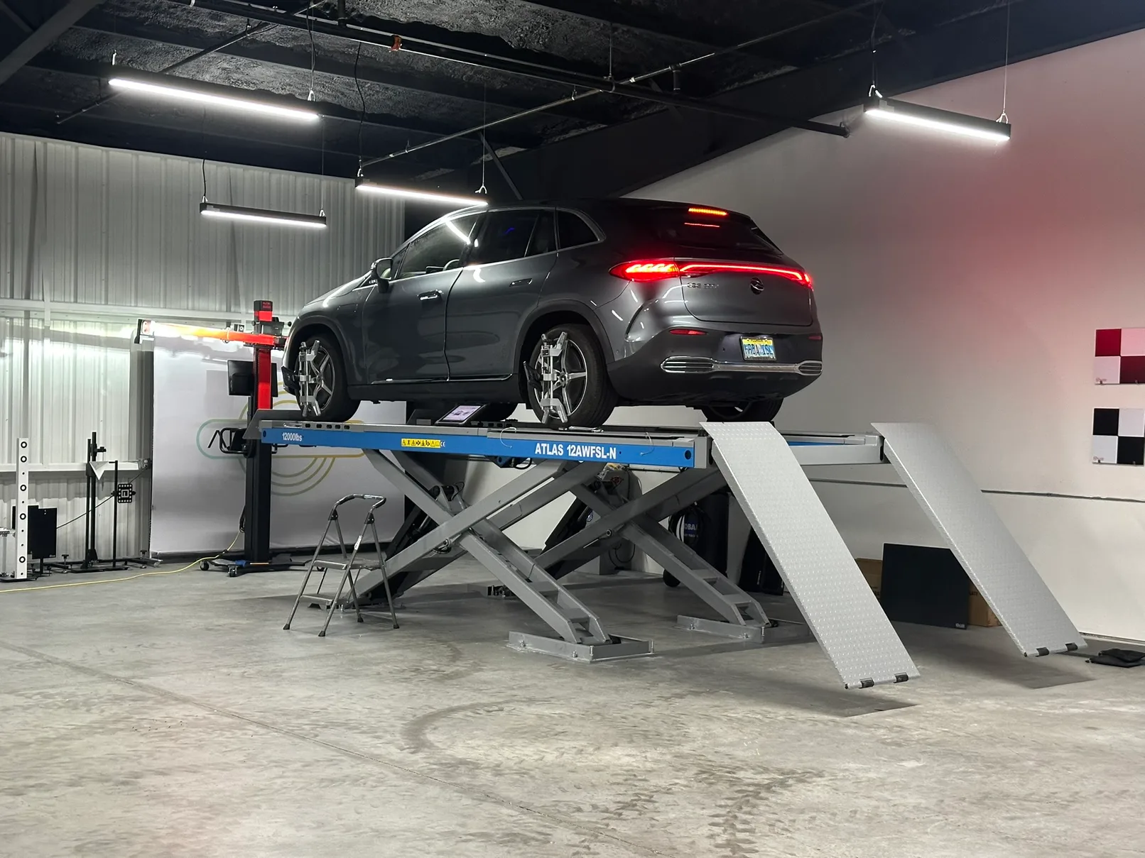 A grey Mercedes SUV raised on a scissor lift with alignment targets clamped to its wheels.