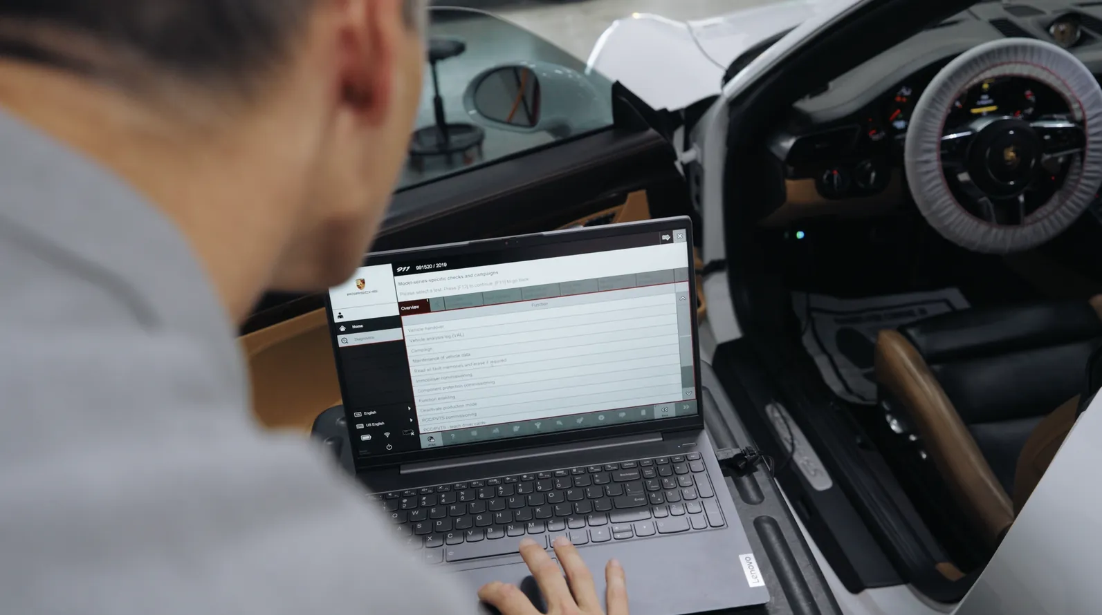 A technician working at a laptop in the open door of a Porsche during a programming session.